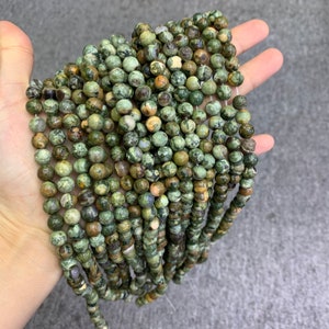 K&ouml;nnte beinhalten: Eine Str&auml;hne aus gr&uuml;nen, braunen und wei&szlig;en Jaspisperlen. Die Perlen sind rund und haben ein gesprenkeltes Muster.