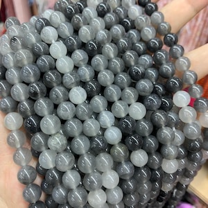 Könnte beinhalten: Nahaufnahme einer Sammlung grauer Edelsteinperlen in verschiedenen Schattierungen. Die Perlen sind rund und glatt, wodurch sie das Licht reflektieren. Geeignet für Schmuckherstellung oder Bastelprojekte.