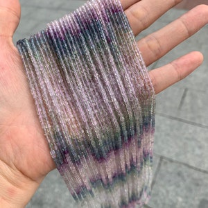 Può includere: Un filo di perline di pietre preziose multicolori. Le perline sono piccole e di forma quadrata. I colori sono sfumature di viola, rosa, verde e blu.