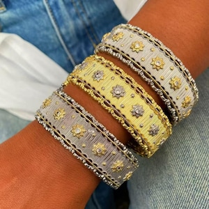 May include: Three wide cuff bracelets featuring a textured, brushed metal finish with scalloped edges. Each bracelet is adorned with repeating star-shaped motifs, with the center of each star set with a small, clear, round gemstone.