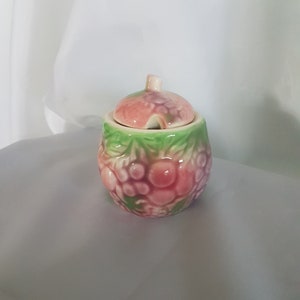 May include: A small ceramic sugar bowl with a lid. The bowl is decorated with a pink and green floral design.