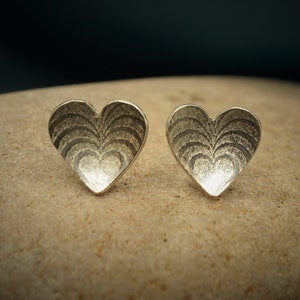 May include: A pair of silver heart-shaped earrings with a textured, concentric circle design.