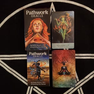 Puede incluir: Un juego de oráculo y una guía con el título "Pathwork Oracle". El juego presenta ilustraciones de figuras y símbolos. La guía y el juego están sobre una superficie negra con un diseño de pentagrama blanco.