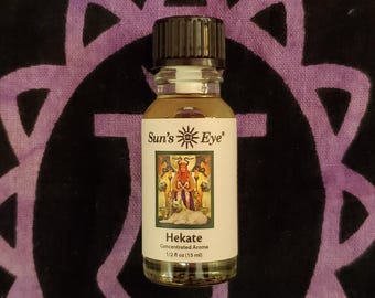 Peut inclure: Petite bouteille en verre d'arôme concentré Hekate de Sun's Eye. L'étiquette présente une illustration d'une figure avec un chien et le texte "Hekate Concentrated Aroma 1/2 fl oz (15 ml)". Le flacon a un bouchon noir.