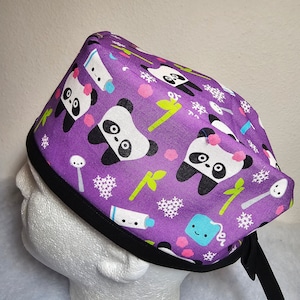 May include: Purple scrub hat with a black trim and a repeating pattern of pandas, snowflakes, toothbrushes, and tea bags.