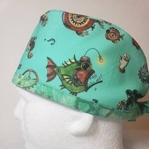 May include: A teal blue surgical scrub hat with a steampunk design featuring a fish with a lightbulb, gears, and other mechanical elements.