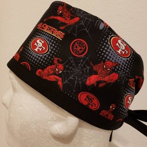 May include: Black scrub hat with a red, white, and black pattern featuring Spider-Man and the San Francisco 49ers logo. The hat has a tie at the back.