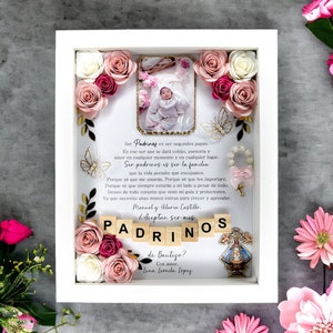 May include: A white frame with a pink and white floral design. The frame contains a photo of a baby girl, a small wooden sign with the text "Aceptan ser mis PADRINOS", and a small image of the Virgin Mary. The text "Ser Padrinos es ser segundos papás. Es ese ser que te dará cobijo, asesoría y amor en cualquier momento y en cualquier lugar. Ser padrinos es ser la familia que la vida permite que escojamos. Porque sé que me amarán. Porque sé que les importaré. Porque sé que siempre estarán a mi lado a pesar de todo. Deseo de todo corazón que sean mi guía y protectores. Ya que necesito unas manos extras para crecer y aprender. Manuel y Hilaria Castillo. de Bautizo? Con amor, Luna Leonila Lopes" is also included in the frame.