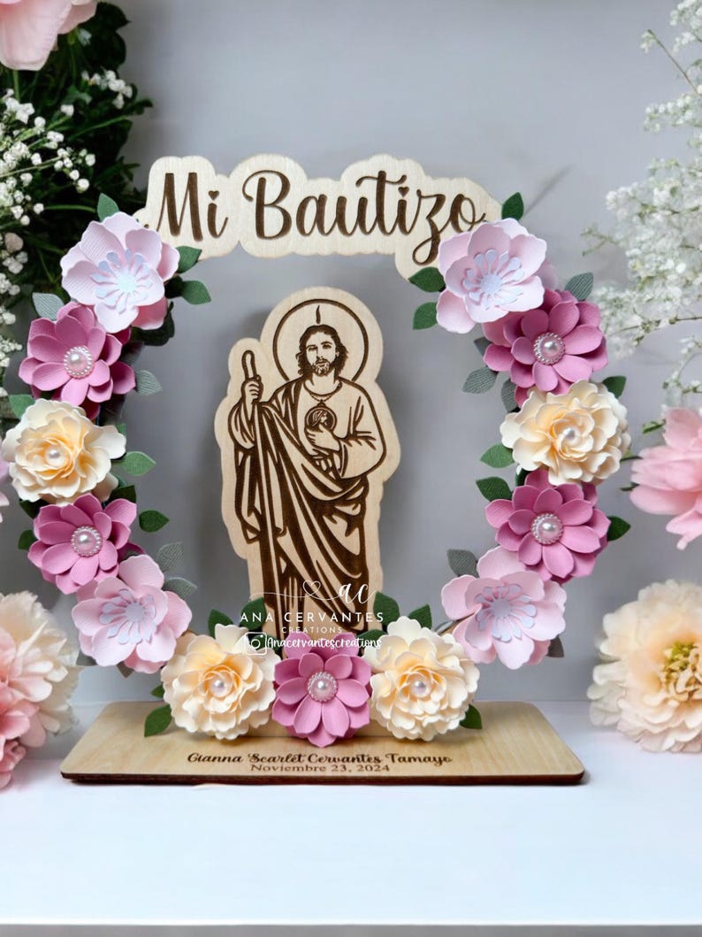 Puede incluir: Un letrero de madera con el texto "Mi Bautizo" en una fuente decorativa, rodeado de una corona de flores de papel rosa y blanco. Una imagen recortada de San Crist&oacute;bal se encuentra en el centro de la corona. El letrero tambi&eacute;n incluye el texto "Gianna Scarlet Cervantes Tamayo, Noviembre 23, 2024".