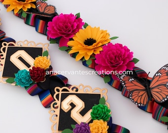 Puede incluir: Primer plano de cintas decorativas con flores y mariposas coloridas. Las cintas tienen una base negra con un patrón de rayas coloridas. Las flores son rosas, amarillas y rojas. Las mariposas son naranjas y negras.