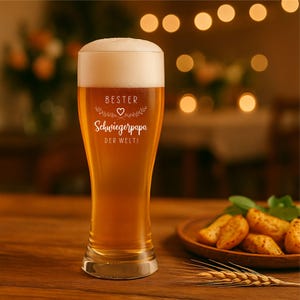 May include: A tall beer glass filled with golden beer and a thick white head. The glass has the words "BESTER Schwiegerpapa DER WELTI" etched on it, with a heart and floral design. A wooden plate with potato wedges and a wheat stalk are in the background.