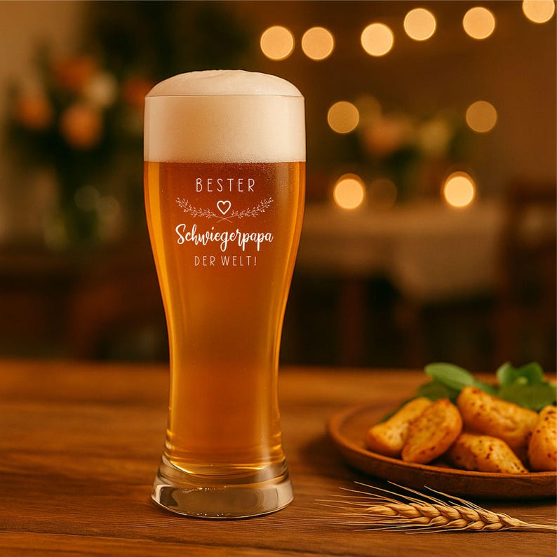 May include: A tall beer glass filled with golden beer and a thick white head. The glass has the words "BESTER Schwiegerpapa DER WELTI" etched on it, with a heart and floral design. A wooden plate with potato wedges and a wheat stalk are in the background.