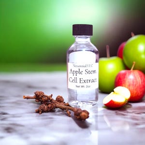 May include: A clear glass bottle with a black cap, labelled "Apple Stem Cell Extract, Net Wt. 2oz." is positioned in front of green and red apples. A small, brown twig lies in front of the bottle on a marble surface.