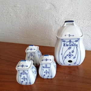 Pode incluir: Um conjunto de potes de especiarias de cerâmica branca com desenhos florais azuis. Os potes estão rotulados como "Paprika", "Nelken" e "Zwiebeln". O maior pote tem uma alça e uma tampa.