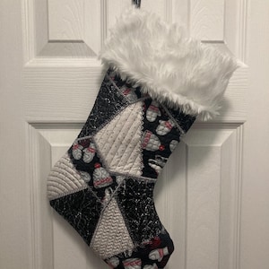 May include: A black and white Christmas stocking with a white faux fur cuff. The stocking is decorated with a patchwork design of various fabrics, including a snowflake pattern and a red and white candy cane pattern.