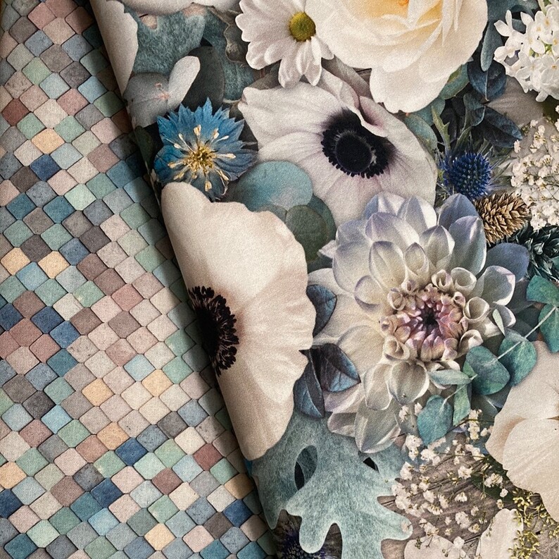 K&ouml;nnte beinhalten: Nahaufnahme eines Blumenstoffes mit einem Muster aus wei&szlig;en, blauen und gr&uuml;nen Blumen. Der Stoff hat eine strukturierte, fast gesteppte Optik.