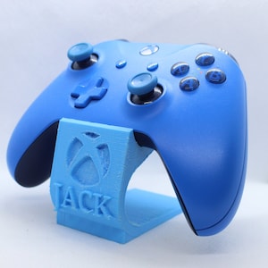 May include: A blue Xbox controller sits on a blue stand with the name "JACK" printed on it.