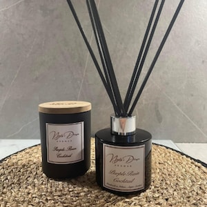 May include: Two black glass bottles with wooden lids and black labels. The labels have white text that reads "Night's Dream Aromas Purple Rain Cocktail". One bottle is a candle and the other is a diffuser with black reeds.