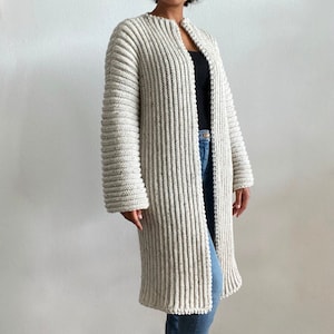 May include: A long, white cardigan with a ribbed texture and a V-neck. The cardigan is open in the front and has long sleeves.