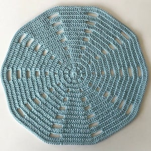 Puede incluir: Un encaje de ganchillo de color azul claro con un diseño circular y detalles calados.