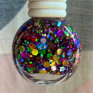 May include: A clear glass bottle filled with colourful glitter. The glitter is a mix of different shapes and sizes, including hexagons, circles, and stars. The glitter is iridescent, meaning it changes colour depending on the angle of light.