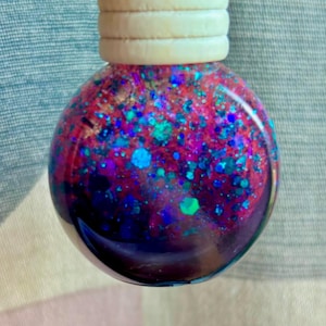 May include: A round glass bauble filled with pink, blue and green glitter. The bauble has a wooden top with a ring for hanging.