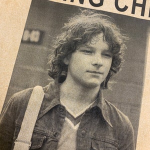 May include: A black and white photo of a young man with long hair, wearing a denim jacket and a white t-shirt. The photo is from a missing person poster. The text on the poster reads "MISSING" and "COUNTY OF DENVER".