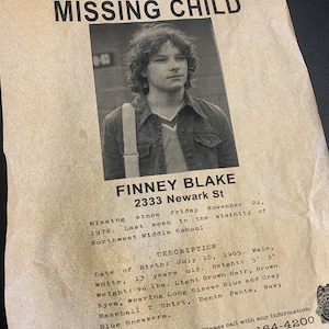 May include: A black and white missing child poster with a photo of a young boy. The poster includes the boy's name, Finney Blake, age, date of birth, height, weight, and clothing description. The poster also includes a phone number to call with any information.