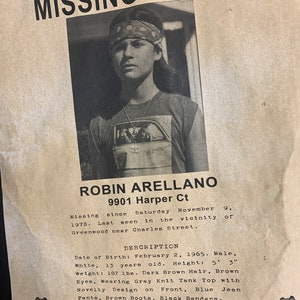May include: A black and white missing child poster with a photo of a young boy wearing a bandana. The poster includes the child's name, Robin Arellano, age, date of birth, and last seen location. The poster also includes a description of the child's appearance and clothing. The poster includes a phone number to call with any information.