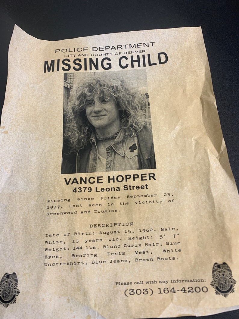 May include: A black and white missing child poster with a photo of a young man with long blond hair. The poster includes the text "Police Department, City and County of Denver, Missing Child, Vance Hopper, 4379 Leona Street, Missing since Friday September 23, 1977. Last seen in the vicinity of Greenwood and Douglas. Description: Date of Birth: August 15, 1962. Male, White, 15 years old. Height: 5' 7" Weight: 144 lbs. Blond Curly Hair, Blue Eyes, Wearing Denim Vest, White Under-shirt, Blue Jeans, Brown Boots. Please call with any Information: (303) 164-4200"