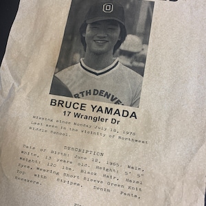 May include: Black and white missing child poster with a photo of a young boy wearing a baseball cap. The poster includes the boy's name, Bruce Yamada, age, 13, and address, 17 Wrangler Dr. The poster also includes a description of the boy's appearance and a phone number to call with any information.