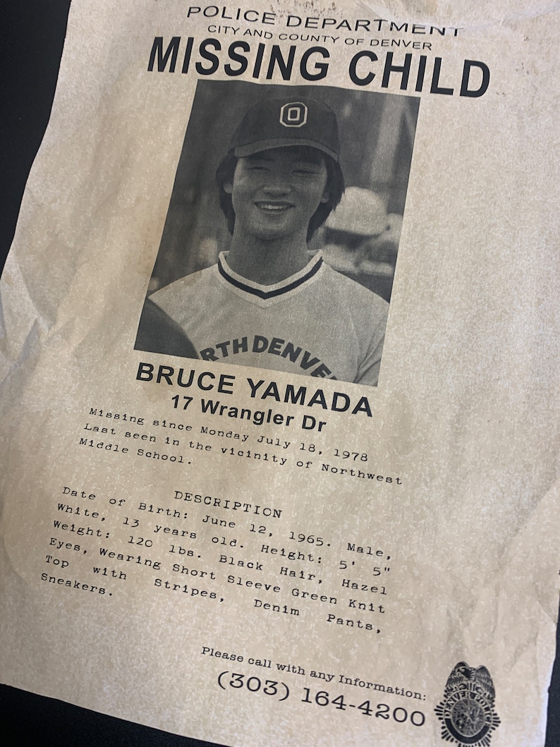 May include: Black and white missing child poster with a photo of a young boy wearing a baseball cap. The poster includes the boy's name, Bruce Yamada, age, 13, and address, 17 Wrangler Dr. The poster also includes a description of the boy's appearance and a phone number to call with any information.