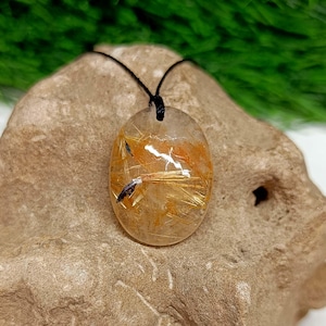 May include: A gold and clear quartz pendant with a black cord. The pendant is oval shaped and has gold flecks throughout.