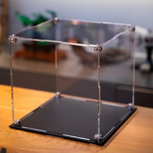 May include: A clear acrylic display case with a black base. The case is made of thick, durable acrylic and has a modern, minimalist design.