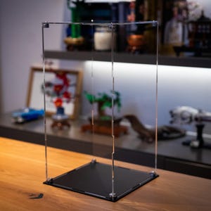 May include: A clear acrylic display case with a black base. The case is empty and ready to display collectibles.