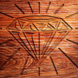 May include: A diamond shape carved into a piece of wood with a sunburst pattern radiating out from the diamond.