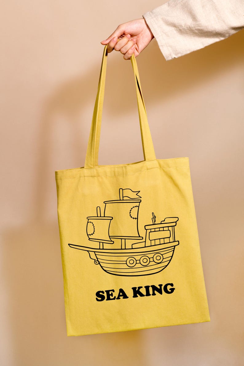 May include: A yellow tote bag with black outlines of a ship and the text "SEA KING".