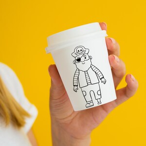 May include: A white paper cup with a black and white illustration of a pirate wearing an eye patch and a hat with a skull and crossbones.