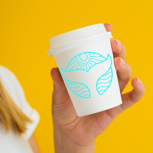 May include: A white to-go coffee cup with a blue line drawing of a whale tail and sun on a yellow background.