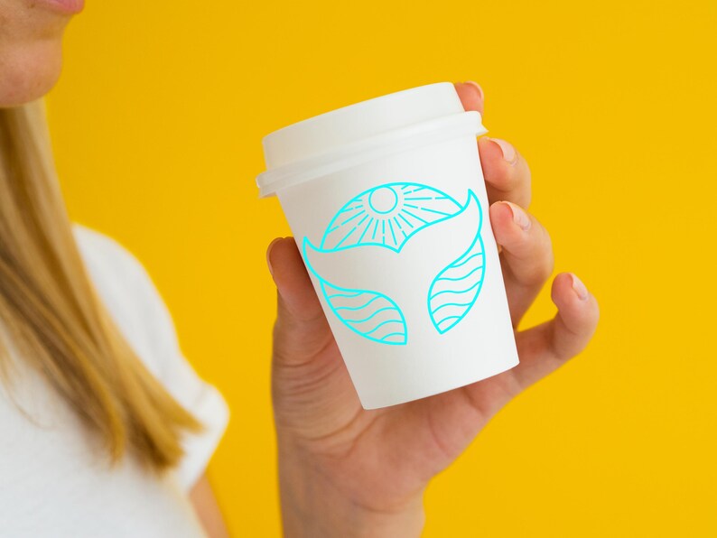 May include: A white to-go coffee cup with a blue line drawing of a whale tail and sun on a yellow background.