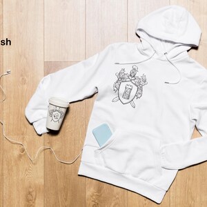 May include: White hooded sweatshirt with a black and white graphic of a coat of arms featuring a sword, shield, and crown. The text "Be Stylish" is visible in the top left corner of the image.