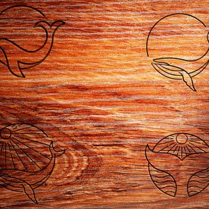 May include: Four different line art designs of a whale with a sun or moon in the background. The designs are on a wooden surface.