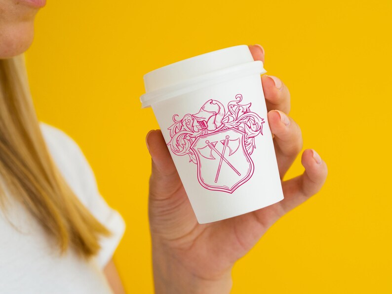 May include: A white to-go coffee cup with a pink and white design of a shield with crossed axes and floral accents.