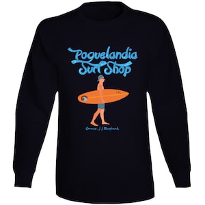 May include: Black long-sleeve t-shirt with a blue and white graphic of a surfer holding a surfboard. The graphic says "Pogue-landia Surf Shop" and "Owner: JJ Maybank".