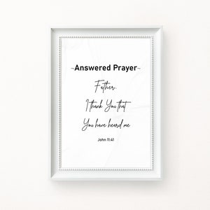 May include: A framed print with the text "~Answered Prayer~ Father. I Thank You that You have heard me" and the Bible verse John 11:41. The text is in black script on a white background, framed in a white frame.