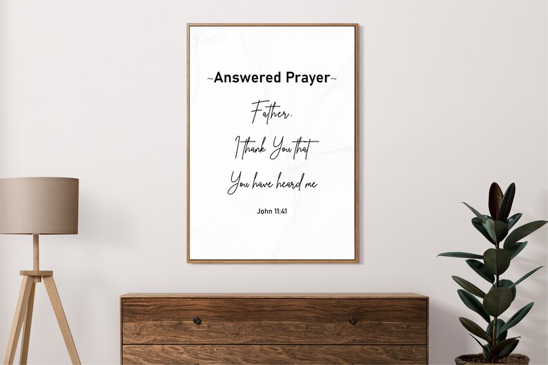 May include: A framed print with the words "Answered Prayer" and a Bible verse. The text is in black script on a white background, framed in a thin gold frame. The print is displayed above a wooden dresser.