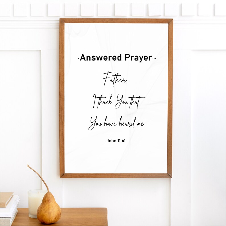 May include: A framed print with the text "Answered Prayer" and a quote from John 11:41. The print has a white background with a subtle pattern and is encased in a brown wooden frame. A pear and candle sit on a wooden surface.