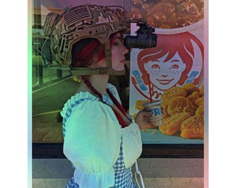 May include: A person wearing a camouflage helmet with an American flag patch and night vision goggles. The person is holding a drink from a fast-food restaurant. The background includes a fast-food restaurant sign.