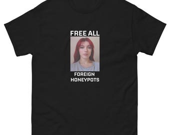 May include: Black t-shirt with the text "FREE ALL FOREIGN HONEYPOTS" above and below a portrait of a woman with red hair. The shirt is made of a soft material.