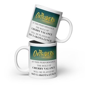 May include: Two white ceramic mugs with the text "The Outsiders A New Musical" in gold and teal. The mugs also state "At this performance, the role of Cherry Valance will be played by Sky Lakota-Lynch."